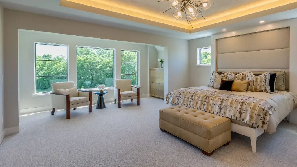 Spacious primary bedroom renovation in Alpharetta featuring a tray ceiling with cove lighting, a custom upholstered headboard wall, and a bright window seating area