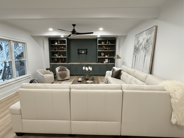 Milton basement remodel with modern living room, off-white sectional, dark green built-in shelves, and light wood flooring.