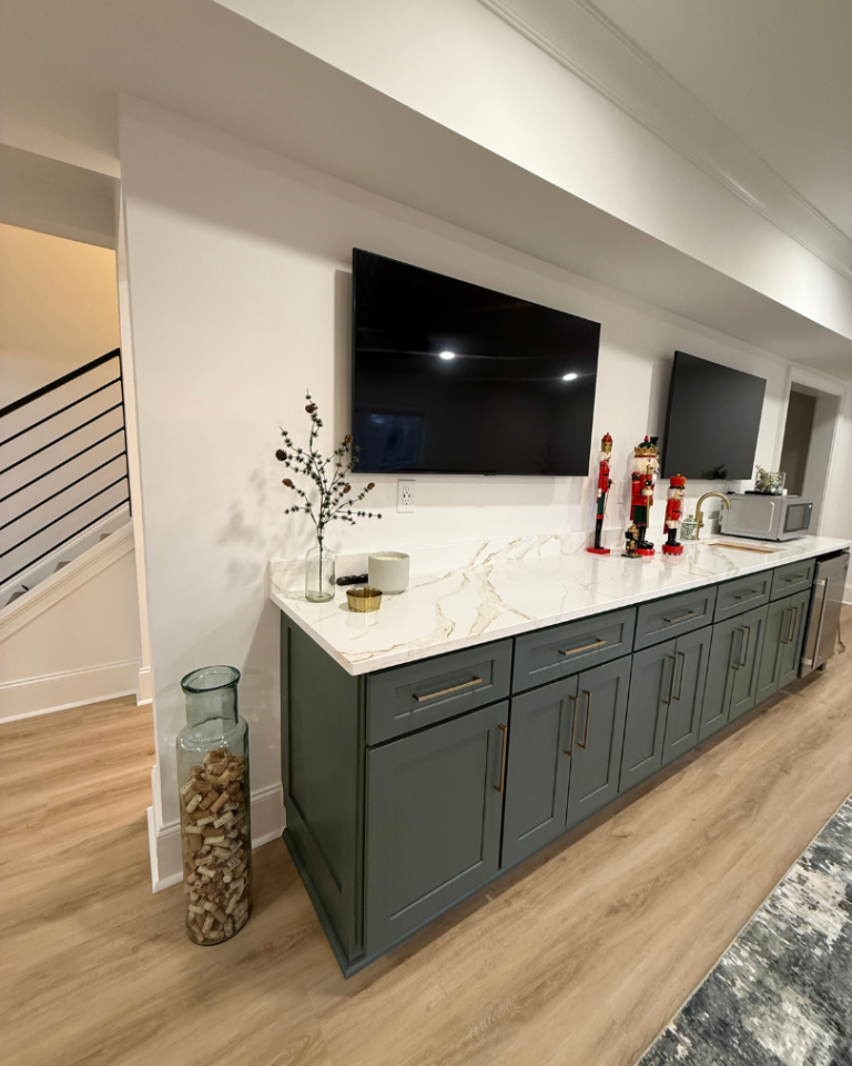 Custom basement wet bar design in Alpharetta with dark green shaker cabinets, gold hardware, and white marble-look quartz countertops.