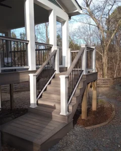Composite decking staircase featuring a modern two-tone railing design with white structural posts and black metal balusters leading up to a covered porch.