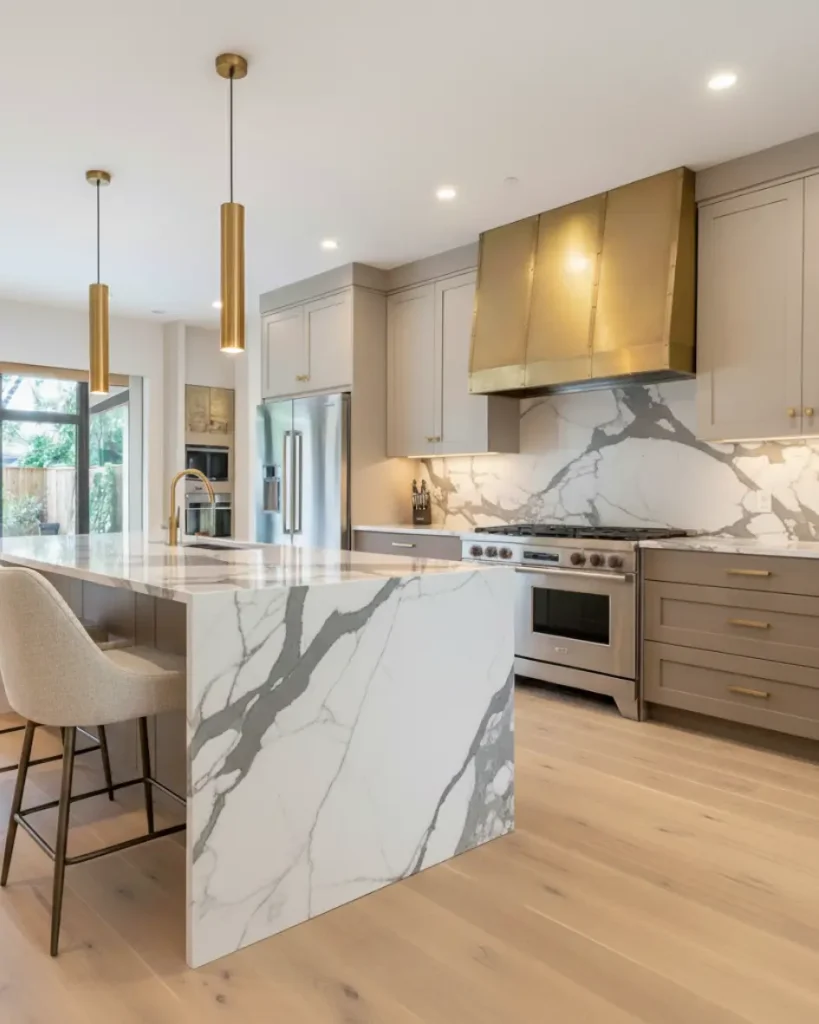 Modern luxury kitchen remodel in North Atlanta featuring a marble waterfall island, matching slab backsplash, and a statement custom brass range hood.