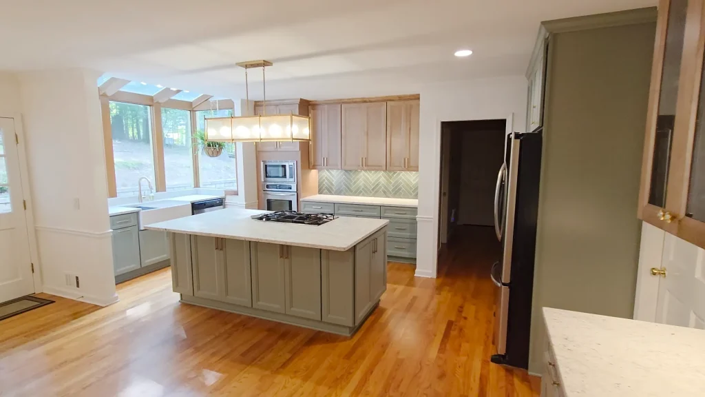 Complete kitchen remodel in North Atlanta featuring a large sage green island with a cooktop, natural wood cabinetry, and sunroom windows.