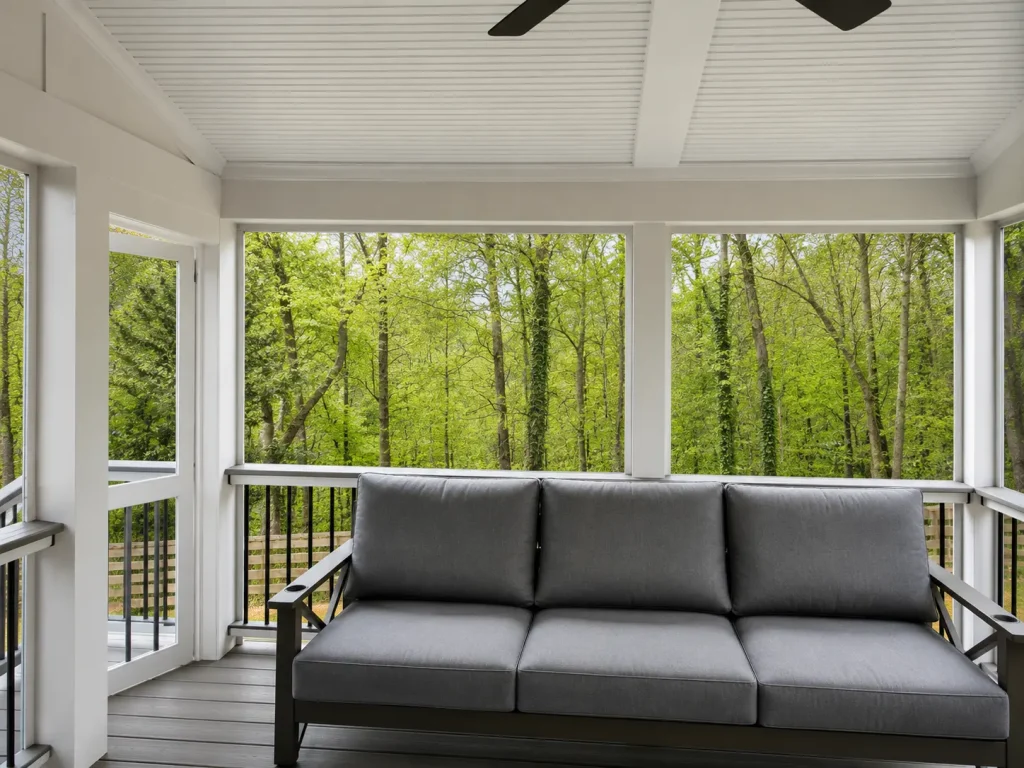 Interior of a completed premium screened porch with composite decking overlooking a wooded backyard in North Atlanta by Yanover Construction.