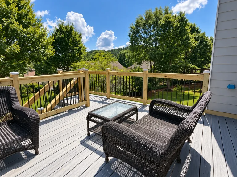 Outdoor seating area on a gray composite deck with natural wood railings and black aluminum balusters overlooking a wooded Cumming, GA backyard.