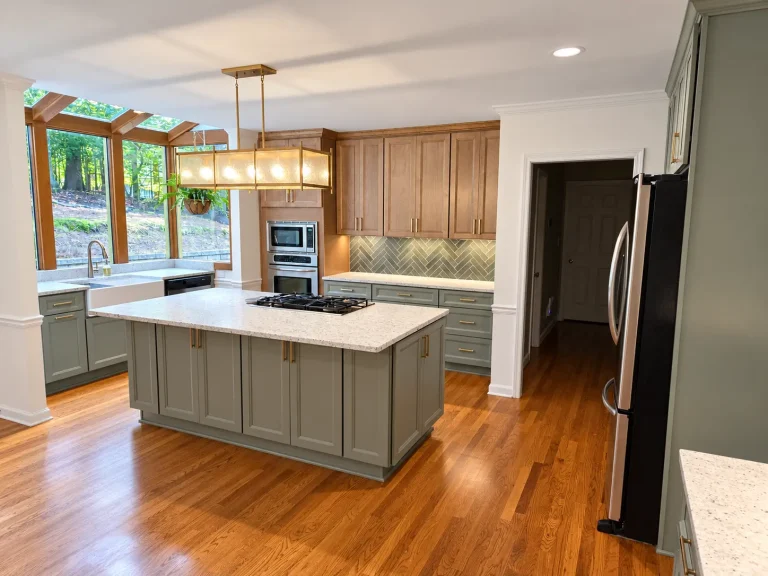 Luxury kitchen remodel in North Metro Atlanta featuring sage green cabinetry, a large quartz island, brass pendant lighting, and a herringbone tile backsplash.